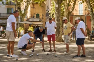 Group of pétanque players chatting around a cochonnet under plane trees on a Provençal square during a golden Mediterranean afternoon.