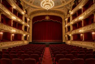 Vue intérieure du Théâtre Saint-Louis de Pau, avec fauteuils rouges, balcons et scène éclairée dans une atmosphère chaleureuse.